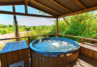 Outdoor hot tub under a wooden roof overlooking lush fields at Scotney Luxury Dome in the United Kingdom.