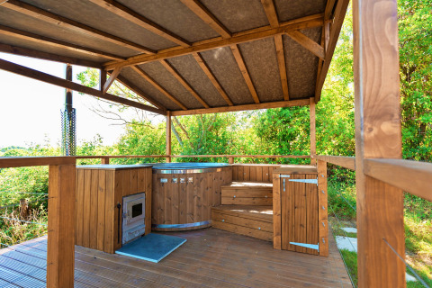 Wooden covered outdoor hot tub with wood burner and steps, surrounded by greenery at Scotney Luxury Dome.