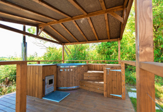 Wooden covered outdoor hot tub with wood burner and steps, surrounded by greenery at Scotney Luxury Dome.