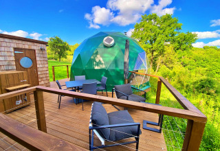 Wooden terrace with modern furniture and a green geodesic dome at Scotney Luxury Dome, United Kingdom.