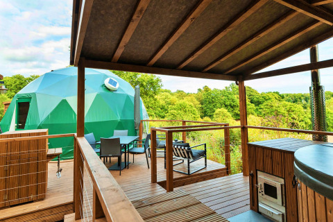 View from a wooden deck with luxury amenities overlooking a green geodesic dome set in a lush landscape.