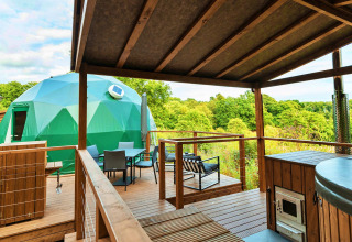 View from a wooden deck with luxury amenities overlooking a green geodesic dome set in a lush landscape.