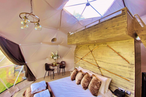 Interior view of Scotney Luxury Dome in the UK featuring a stylish bed, loft space, and modern lighting.