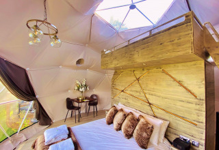 Interior view of Scotney Luxury Dome in the UK featuring a stylish bed, loft space, and modern lighting.