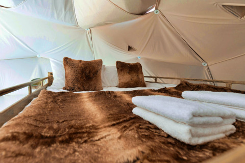 Close-up of a bed with brown cushions and a blanket inside the Scotney Luxury Dome in the UK.
