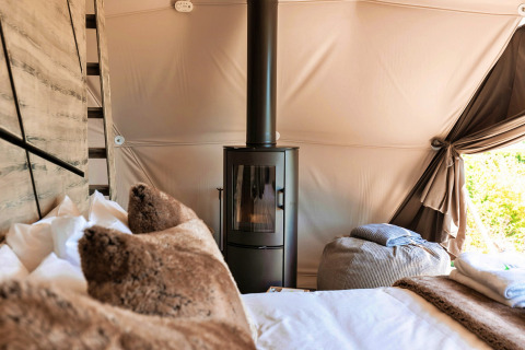 Interior of Scotney Luxury Dome in the UK, showing a wood stove, plush pillows, and a cozy, bright atmosphere.
