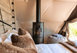 Interior of Scotney Luxury Dome in the UK, showing a wood stove, plush pillows, and a cozy, bright atmosphere.