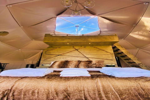 Interior of Scotney Luxury Dome in the UK with plush bed, wooden decor, and skylight showing blue sky.