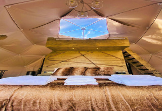 Interior of Scotney Luxury Dome in the UK with plush bed, wooden decor, and skylight showing blue sky.