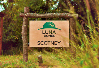 Wooden sign reads 'LUNA DOMES SCOTNEY' with green dome logo in a lush UK outdoor setting.