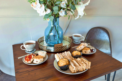 Afternoon tea with sandwiches, scones, muffins and tea on table with flowers in Scotney Luxury Dome UK.