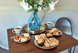 Afternoon tea with sandwiches, scones, muffins and tea on table with flowers in Scotney Luxury Dome UK.