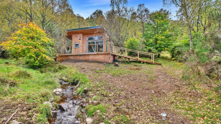 Cosagach Falls Cabin, een houten chalet in het bos met een beekje dat voor de deur stroomt.