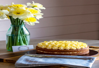 Une table avec un vase de jonquilles jaunes et un gâteau à la crème au citron joliment décoré.