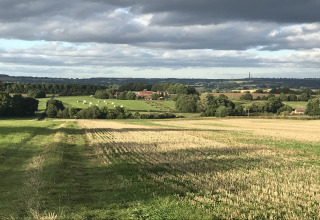 View from The Campion pod in the UK overlooking farmlands, trees, hay bales, and cloudy dramatic sky.