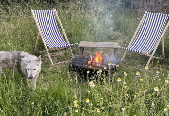 Espace extérieur d’un pod avec deux chaises longues rayées, un feu, une table et un chien dans l’herbe.