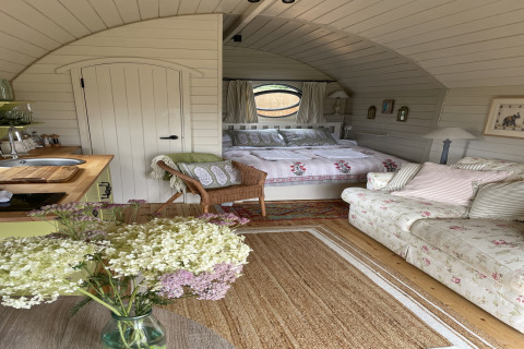 Cozy interior of 'The Campion' pod in the UK featuring a bed, floral sofa, kitchenette, and rustic decor.