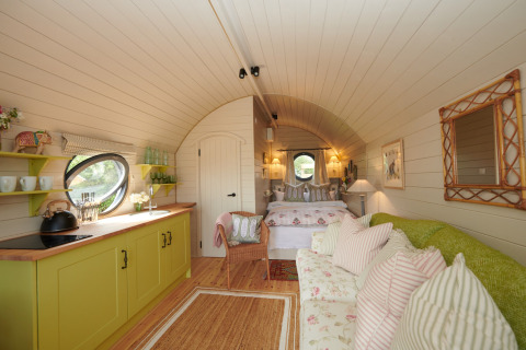 Cozy interior of The Campion pod in the UK featuring a kitchenette, sofa, colorful pillows, and a bed.