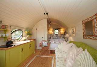 Cozy interior of The Campion pod in the UK featuring a kitchenette, sofa, colorful pillows, and a bed.