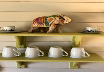 Étagère dans The Campion pod avec éléphant décoratif, deux tasses avec soucoupes et quatre mugs blancs.