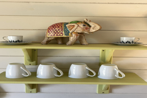 Shelf in The Campion pod with a decorative elephant, two cups with saucers, and four white mugs below.