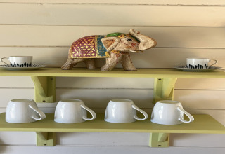 Shelf in The Campion pod with a decorative elephant, two cups with saucers, and four white mugs below.