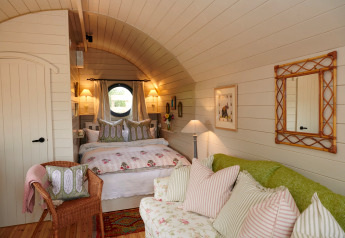 Chambre douillette du pod The Campion au Royaume-Uni, décor champêtre, coussins moelleux et ambiance chaleureuse.