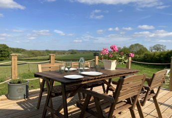 Terrasse en bois avec table dressée, fleurs et vue sur la campagne au pod The Campion, Royaume-Uni.