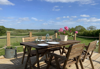 Wooden terrace with set dining table, flowers, and countryside view at The Campion pod in the United Kingdom.