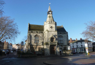 Historisch stadhuis met een kloktoren in het centrum, bomen en winkels op een zonnige dag in de stad.