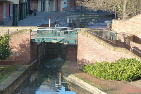 Foto van een rustige kanaalsluis met een brug in een stedelijk gebied, omringd door bakstenen muren en planten.