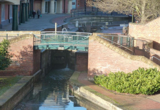 Foto van een rustige kanaalsluis met een brug in een stedelijk gebied, omringd door bakstenen muren en planten.