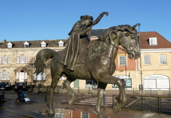 Statue équestre sur une place de ville entourée de bâtiments historiques sous un ciel bleu clair.
