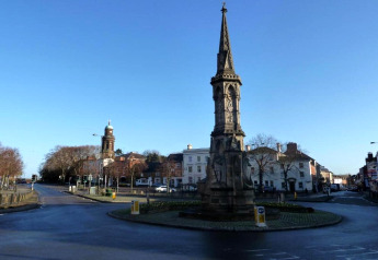 Photo d’un monument en pierre au centre d’un rond-point dans une ville tranquille sous un ciel bleu.