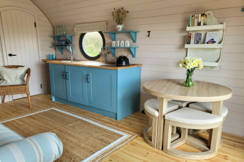 Sfeervolle keuken in The Cornflower pod, Verenigd Koninkrijk, met blauwe kasten en ronde houten tafel.
