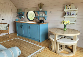 Sfeervolle keuken in The Cornflower pod, Verenigd Koninkrijk, met blauwe kasten en ronde houten tafel.