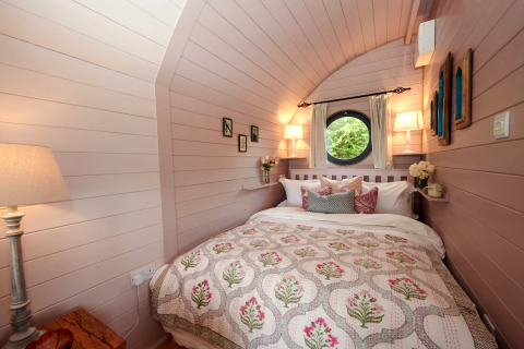 Chambre douillette dans la pod 'The Cornflower' au Royaume-Uni, avec fenêtre ronde et lits moelleux.