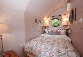 Sfeervolle slaapkamer in 'The Cornflower'-pod in het Verenigd Koninkrijk met rond raam en comfortabele bedden.