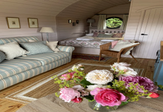 Intérieur chaleureux du pod The Cornflower avec canapé rayé, fleurs fraîches et lit douillet au Royaume-Uni.