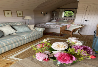 Intérieur chaleureux du pod The Cornflower avec canapé rayé, fleurs fraîches et lit douillet au Royaume-Uni.