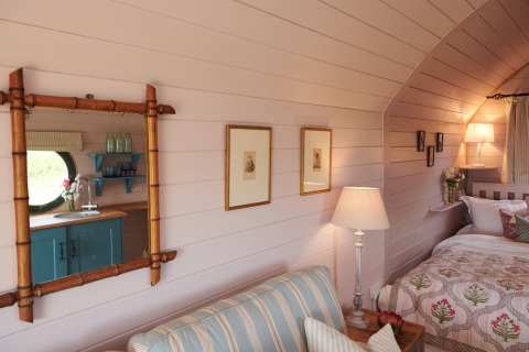 Sfeervol interieur in de Engelse pod 'The Cornflower', met bed, bank, lamp en houten wand.