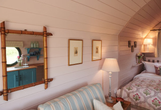 Sfeervol interieur in de Engelse pod 'The Cornflower', met bed, bank, lamp en houten wand.