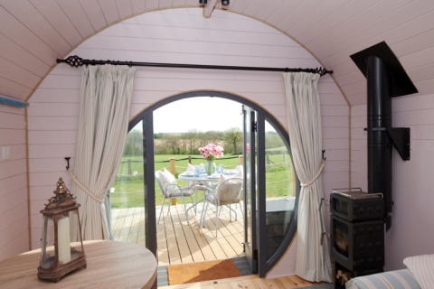 Interieur van The Cornflower pod met ronde deuren naar een terras en uitzicht op groene velden.