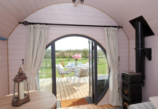Interieur van The Cornflower pod met ronde deuren naar een terras en uitzicht op groene velden.