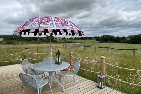 Buitenterras met tafel, stoelen en kleurrijke parasol bij The Cornflower pod in het Britse platteland.