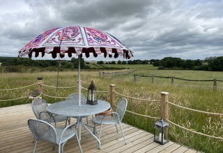 Buitenterras met tafel, stoelen en kleurrijke parasol bij The Cornflower pod in het Britse platteland.