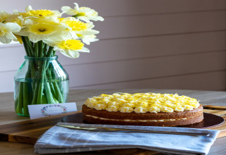 Taart met gele topping en narcissen in vaas op houten tafel bij The Cornflower pod in het Verenigd Koninkrijk.