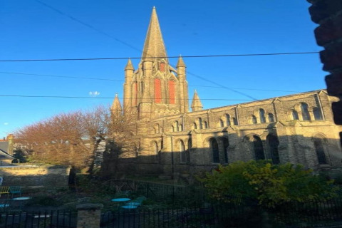 Uitzicht vanuit een pod op een grote gotische kerk met hoge torenspits, blauwe lucht en tuin op de voorgrond.