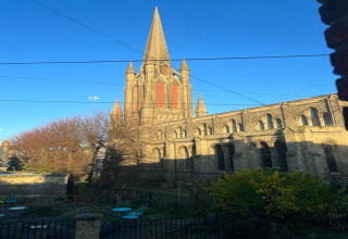 Uitzicht vanuit een pod op een grote gotische kerk met hoge torenspits, blauwe lucht en tuin op de voorgrond.