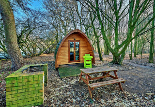 Træ glamping pod i Suffolk Woodland Retreat, Storbritannien, omgivet af træer med picnicbord og grill.